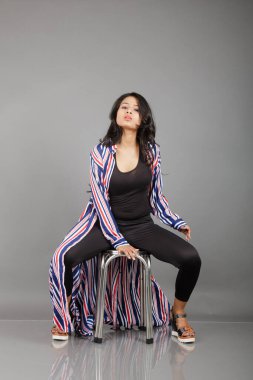 Dişi bir dansçı metal bir taburede oturur, çizgili uzun paltosu etrafında dönerken canlı ve anlamlı bir poz verir. Moda, yaşam tarzı, güçlendirme ve yaratıcı hareket kavramları için mükemmel..