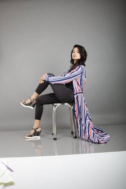 Dişi bir dansçı metal bir taburede oturur, çizgili uzun paltosu etrafında dönerken canlı ve anlamlı bir poz verir. Moda, yaşam tarzı, güçlendirme ve yaratıcı hareket kavramları için mükemmel..