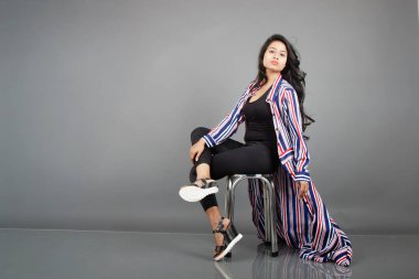 Dişi bir dansçı metal bir taburede oturur, çizgili uzun paltosu etrafında dönerken canlı ve anlamlı bir poz verir. Moda, yaşam tarzı, güçlendirme ve yaratıcı hareket kavramları için mükemmel..