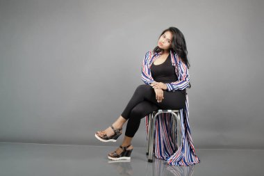 Dişi bir dansçı metal bir taburede oturur, çizgili uzun paltosu etrafında dönerken canlı ve anlamlı bir poz verir. Moda, yaşam tarzı, güçlendirme ve yaratıcı hareket kavramları için mükemmel..