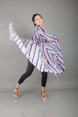 Siyah tayt, topuklu, siyah üst ve kırmızı, mavi ve beyaz çizgili tunik giyen güzel, genç bir kadın. Gülüyor, dönüyor, zıplıyor, neşeyle dans ediyor ve bir tabureyle poz veriyor.