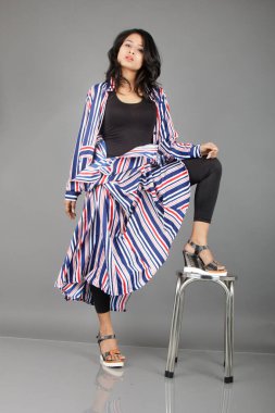 Siyah tayt, topuklu, siyah üst ve kırmızı, mavi ve beyaz çizgili tunik giyen güzel, genç bir kadın. Gülüyor, dönüyor, zıplıyor, neşeyle dans ediyor ve bir tabureyle poz veriyor.