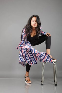 Şık bir kadın koyu mavi, kırmızı ve beyaz çizgili bir ceketle hareketli, özgüvenli, dengeli ve dinamik moda enerjisini vurgulayarak, siyah bir kıyafet ve topuklu üzerinde canlı bir dans pozu verir.