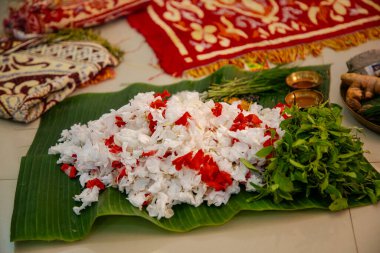 Canlı kırmızı ve beyaz çiçekler, taze fesleğen yaprakları (Tulsi) ve bir Hindu puja ayini için muz yapraklarında sergilenen diğer kutsal eşyalar..