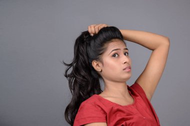 Kırmızı bluz ve mavi kot giyen kendine güvenen genç bir kadın neşeli yüz ifadeleri ve duygularıyla poz veriyor.