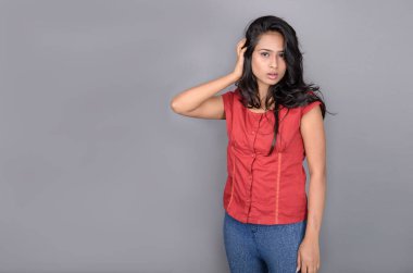 Kırmızı bluz ve mavi kot giyen kendine güvenen genç bir kadın neşeli yüz ifadeleri ve duygularıyla poz veriyor.