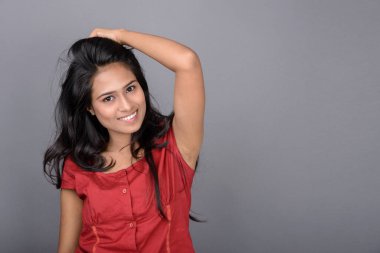 Kırmızı bluz ve mavi kot giyen kendine güvenen genç bir kadın neşeli yüz ifadeleri ve duygularıyla poz veriyor.