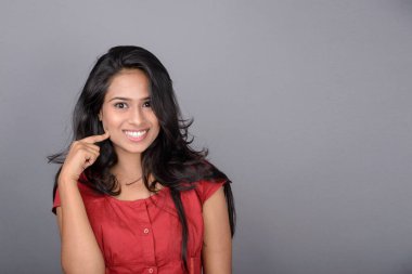 Kırmızı bluz ve mavi kot giyen kendine güvenen genç bir kadın neşeli yüz ifadeleri ve duygularıyla poz veriyor.