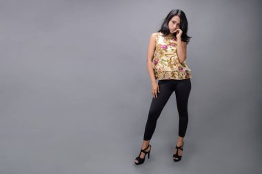 Çiçekli bir bluz, siyah tayt ve siyah topuklu giyen çekici genç bir kadın, neşeli yüz ifadeleri ve farklı duygularla poz veriyor, modern tarzı, zarafeti sergiliyor..