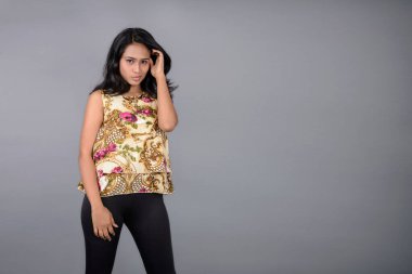 Çiçekli bir bluz, siyah tayt ve siyah topuklu giyen çekici genç bir kadın, neşeli yüz ifadeleri ve farklı duygularla poz veriyor, modern tarzı, zarafeti sergiliyor..