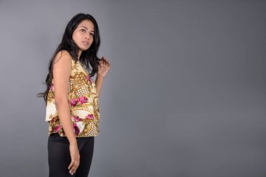 Çiçekli bir bluz, siyah tayt ve siyah topuklu giyen çekici genç bir kadın, neşeli yüz ifadeleri ve farklı duygularla poz veriyor, modern tarzı, zarafeti sergiliyor..