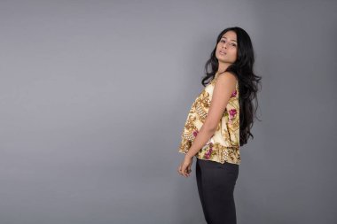 Çiçekli bir bluz, siyah tayt ve siyah topuklu giyen çekici genç bir kadın, neşeli yüz ifadeleri ve farklı duygularla poz veriyor, modern tarzı, zarafeti sergiliyor..