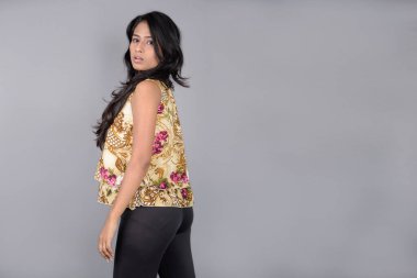 Çiçekli bir bluz, siyah tayt ve siyah topuklu giyen çekici genç bir kadın, neşeli yüz ifadeleri ve farklı duygularla poz veriyor, modern tarzı, zarafeti sergiliyor..