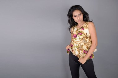 Çiçekli bir bluz, siyah tayt ve siyah topuklu giyen çekici genç bir kadın, neşeli yüz ifadeleri ve farklı duygularla poz veriyor, modern tarzı, zarafeti sergiliyor..