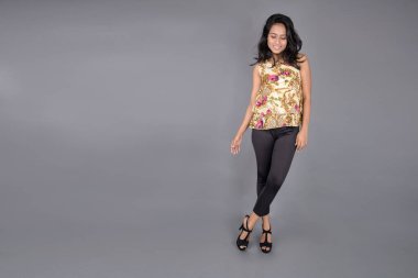 Çiçekli bir bluz, siyah tayt ve siyah topuklu giyen çekici genç bir kadın, neşeli yüz ifadeleri ve farklı duygularla poz veriyor, modern tarzı, zarafeti sergiliyor..