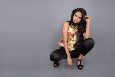 Çiçekli bir bluz, siyah tayt ve siyah topuklu giyen çekici genç bir kadın, neşeli yüz ifadeleri ve farklı duygularla poz veriyor, modern tarzı, zarafeti sergiliyor..