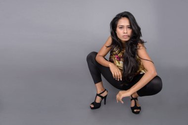 Çiçekli bir bluz, siyah tayt ve siyah topuklu giyen çekici genç bir kadın, neşeli yüz ifadeleri ve farklı duygularla poz veriyor, modern tarzı, zarafeti sergiliyor..