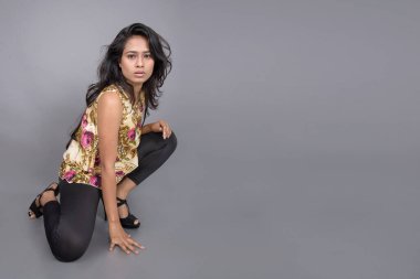 Çiçekli bir bluz, siyah tayt ve siyah topuklu giyen çekici genç bir kadın, neşeli yüz ifadeleri ve farklı duygularla poz veriyor, modern tarzı, zarafeti sergiliyor..