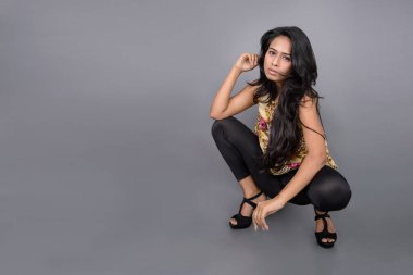 Çiçekli bir bluz, siyah tayt ve siyah topuklu giyen çekici genç bir kadın, neşeli yüz ifadeleri ve farklı duygularla poz veriyor, modern tarzı, zarafeti sergiliyor..