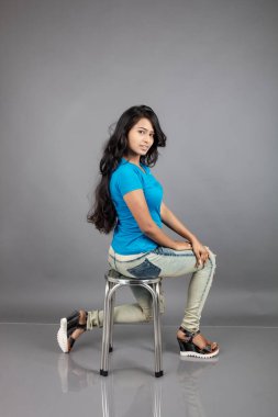 Genç bir kadın özgüvenle mavi tişört, sıkıntılı kot pantolon, topuklu ayakkabı giyerek poz veriyor, cazibe ve zarafetle gelişigüzel bir şehir tarzı sergiliyor, saç bakımı, özgürlük, kendini ifade etme projesi için uygun.