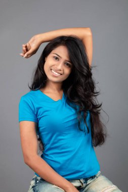 Genç bir kadın özgüvenle mavi tişört, sıkıntılı kot pantolon, topuklu ayakkabı giyerek poz veriyor, cazibe ve zarafetle gelişigüzel bir şehir tarzı sergiliyor, saç bakımı, özgürlük, kendini ifade etme projesi için uygun.