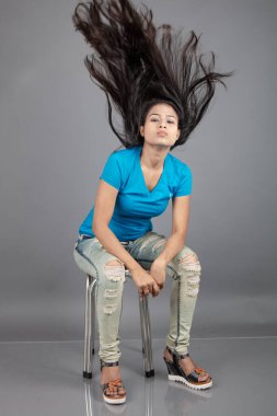 Genç bir kadın özgüvenle mavi tişört, sıkıntılı kot pantolon, topuklu ayakkabı giyerek poz veriyor, cazibe ve zarafetle gelişigüzel bir şehir tarzı sergiliyor, saç bakımı, özgürlük, kendini ifade etme projesi için uygun.