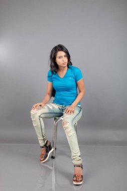 Genç bir kadın özgüvenle mavi tişört, sıkıntılı kot pantolon, topuklu ayakkabı giyerek poz veriyor, cazibe ve zarafetle gelişigüzel bir şehir tarzı sergiliyor, saç bakımı, özgürlük, kendini ifade etme projesi için uygun.