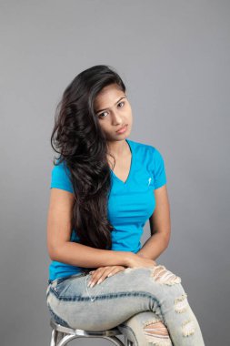 Genç bir kadın özgüvenle mavi tişört, sıkıntılı kot pantolon, topuklu ayakkabı giyerek poz veriyor, cazibe ve zarafetle gelişigüzel bir şehir tarzı sergiliyor, saç bakımı, özgürlük, kendini ifade etme projesi için uygun.