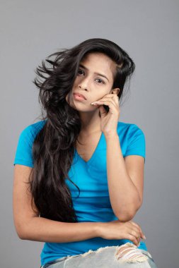 Genç bir kadın özgüvenle mavi tişört, sıkıntılı kot pantolon, topuklu ayakkabı giyerek poz veriyor, cazibe ve zarafetle gelişigüzel bir şehir tarzı sergiliyor, saç bakımı, özgürlük, kendini ifade etme projesi için uygun.