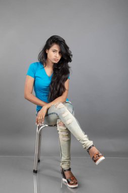 Genç bir kadın özgüvenle mavi tişört, sıkıntılı kot pantolon, topuklu ayakkabı giyerek poz veriyor, cazibe ve zarafetle gelişigüzel bir şehir tarzı sergiliyor, saç bakımı, özgürlük, kendini ifade etme projesi için uygun.