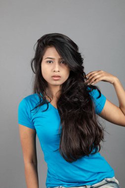 Genç bir kadın özgüvenle mavi tişört, sıkıntılı kot pantolon, topuklu ayakkabı giyerek poz veriyor, cazibe ve zarafetle gelişigüzel bir şehir tarzı sergiliyor, saç bakımı, özgürlük, kendini ifade etme projesi için uygun.