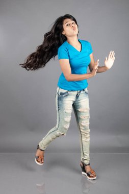 Genç bir kadın özgüvenle mavi tişört, sıkıntılı kot pantolon, topuklu ayakkabı giyerek poz veriyor, cazibe ve zarafetle gelişigüzel bir şehir tarzı sergiliyor, saç bakımı, özgürlük, kendini ifade etme projesi için uygun.