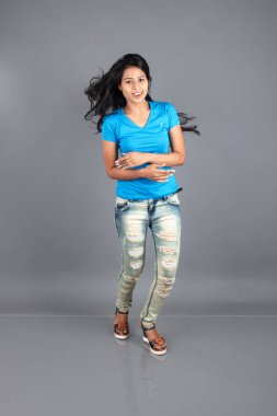 Genç bir kadın özgüvenle mavi tişört, sıkıntılı kot pantolon, topuklu ayakkabı giyerek poz veriyor, cazibe ve zarafetle gelişigüzel bir şehir tarzı sergiliyor, saç bakımı, özgürlük, kendini ifade etme projesi için uygun.