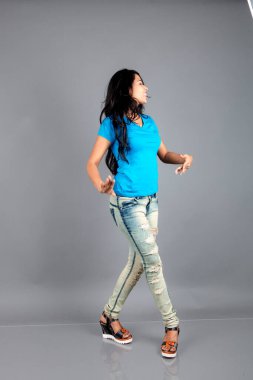 Genç bir kadın özgüvenle mavi tişört, sıkıntılı kot pantolon, topuklu ayakkabı giyerek poz veriyor, cazibe ve zarafetle gelişigüzel bir şehir tarzı sergiliyor, saç bakımı, özgürlük, kendini ifade etme projesi için uygun.