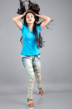 Genç bir kadın özgüvenle mavi tişört, sıkıntılı kot pantolon, topuklu ayakkabı giyerek poz veriyor, cazibe ve zarafetle gelişigüzel bir şehir tarzı sergiliyor, saç bakımı, özgürlük, kendini ifade etme projesi için uygun.