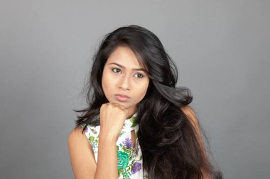 Kendine güvenen, çiçekli bluz giyen genç bir kadın zarif bir şekilde stüdyo ortamında poz veriyor. Güzelliğini, kendine güvenini ve tarzını sergiliyor. Onun uzun saçları zarif bir şekilde akıyor, resme hareketlilik ve canlılık katıyor.