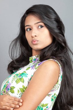 Kendine güvenen, çiçekli bluz giyen genç bir kadın zarif bir şekilde stüdyo ortamında poz veriyor. Güzelliğini, kendine güvenini ve tarzını sergiliyor. Onun uzun saçları zarif bir şekilde akıyor, resme hareketlilik ve canlılık katıyor.