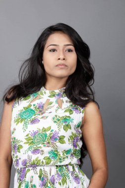 Kendine güvenen, çiçekli bluz giyen genç bir kadın zarif bir şekilde stüdyo ortamında poz veriyor. Güzelliğini, kendine güvenini ve tarzını sergiliyor. Onun uzun saçları zarif bir şekilde akıyor, resme hareketlilik ve canlılık katıyor.