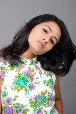 Kendine güvenen, çiçekli bluz giyen genç bir kadın zarif bir şekilde stüdyo ortamında poz veriyor. Güzelliğini, kendine güvenini ve tarzını sergiliyor. Onun uzun saçları zarif bir şekilde akıyor, resme hareketlilik ve canlılık katıyor.