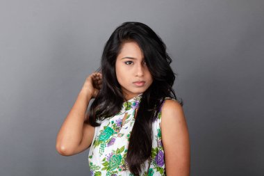 Kendine güvenen, çiçekli bluz giyen genç bir kadın zarif bir şekilde stüdyo ortamında poz veriyor. Güzelliğini, kendine güvenini ve tarzını sergiliyor. Onun uzun saçları zarif bir şekilde akıyor, resme hareketlilik ve canlılık katıyor.