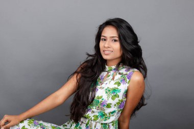 Kendine güvenen, çiçekli bluz giyen genç bir kadın zarif bir şekilde stüdyo ortamında poz veriyor. Güzelliğini, kendine güvenini ve tarzını sergiliyor. Onun uzun saçları zarif bir şekilde akıyor, resme hareketlilik ve canlılık katıyor.