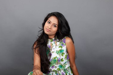 Kendine güvenen, çiçekli bluz giyen genç bir kadın zarif bir şekilde stüdyo ortamında poz veriyor. Güzelliğini, kendine güvenini ve tarzını sergiliyor. Onun uzun saçları zarif bir şekilde akıyor, resme hareketlilik ve canlılık katıyor.