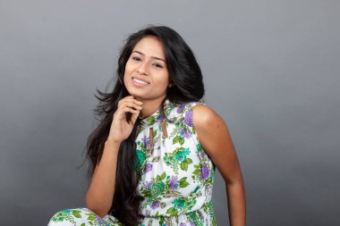 Kendine güvenen, çiçekli bluz giyen genç bir kadın zarif bir şekilde stüdyo ortamında poz veriyor. Güzelliğini, kendine güvenini ve tarzını sergiliyor. Onun uzun saçları zarif bir şekilde akıyor, resme hareketlilik ve canlılık katıyor.