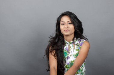 Kendine güvenen, çiçekli bluz giyen genç bir kadın zarif bir şekilde stüdyo ortamında poz veriyor. Güzelliğini, kendine güvenini ve tarzını sergiliyor. Onun uzun saçları zarif bir şekilde akıyor, resme hareketlilik ve canlılık katıyor.