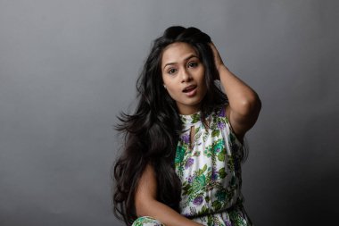 Kendine güvenen, çiçekli bluz giyen genç bir kadın zarif bir şekilde stüdyo ortamında poz veriyor. Güzelliğini, kendine güvenini ve tarzını sergiliyor. Onun uzun saçları zarif bir şekilde akıyor, resme hareketlilik ve canlılık katıyor.