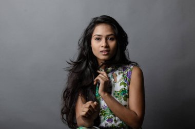 Kendine güvenen, çiçekli bluz giyen genç bir kadın zarif bir şekilde stüdyo ortamında poz veriyor. Güzelliğini, kendine güvenini ve tarzını sergiliyor. Onun uzun saçları zarif bir şekilde akıyor, resme hareketlilik ve canlılık katıyor.