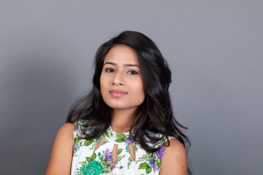 Kendine güvenen, çiçekli bluz giyen genç bir kadın zarif bir şekilde stüdyo ortamında poz veriyor. Güzelliğini, kendine güvenini ve tarzını sergiliyor. Onun uzun saçları zarif bir şekilde akıyor, resme hareketlilik ve canlılık katıyor.