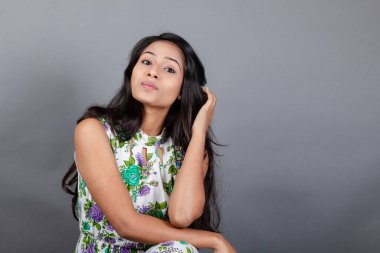 Kendine güvenen, çiçekli bluz giyen genç bir kadın zarif bir şekilde stüdyo ortamında poz veriyor. Güzelliğini, kendine güvenini ve tarzını sergiliyor. Onun uzun saçları zarif bir şekilde akıyor, resme hareketlilik ve canlılık katıyor.