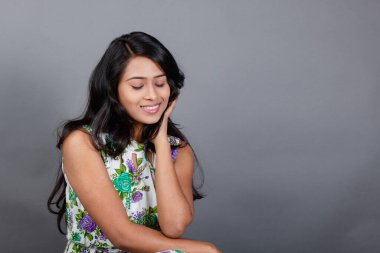 Kendine güvenen, çiçekli bluz giyen genç bir kadın zarif bir şekilde stüdyo ortamında poz veriyor. Güzelliğini, kendine güvenini ve tarzını sergiliyor. Onun uzun saçları zarif bir şekilde akıyor, resme hareketlilik ve canlılık katıyor.