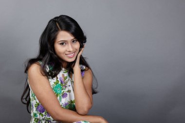 Kendine güvenen, çiçekli bluz giyen genç bir kadın zarif bir şekilde stüdyo ortamında poz veriyor. Güzelliğini, kendine güvenini ve tarzını sergiliyor. Onun uzun saçları zarif bir şekilde akıyor, resme hareketlilik ve canlılık katıyor.